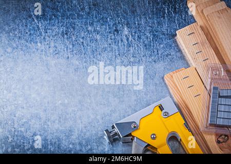 Die gelbe Heftpistole heftet Holzbohlen auf metallischem Hintergrund. Stockfoto