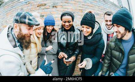 Große, multiethnische Gruppe von Kindern, die sich auf ihrem Smartphone Videos ansehen. Männer und Frauen lachen, Spaß haben. Moment der Leichtigkeit A Stockfoto