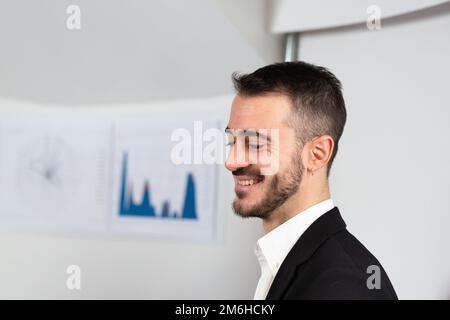 Junger, neu angestellter Unternehmer, der mit seinem Erfolg zufrieden ist. Finanzdiagramme auf weißem Hintergrund und große Werbetexte Stockfoto
