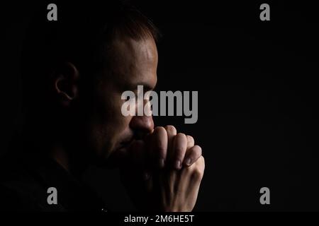 Nahaufnahme eines treuen, erwachsenen Mannes, der betet, Hände in Gottesfurcht gefaltet mit dem Kopf nach unten und Augen geschlossen in religiösem Eifer. Schwarzer Hintergrund. Konzept Stockfoto