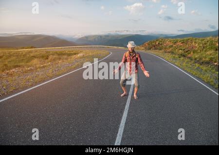 Ein lächelnder, bärtiger, freundlicher weißer Mann in Hemd und Shorts mit Rucksack begrüßt Sie, wenn Sie seine Arme seitlich strecken und sitzen Stockfoto