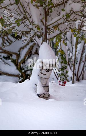 Verschneite Skulptur im Garten, viel Schnee auf Pflanzen und eine Holzfigur Stockfoto