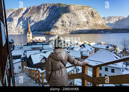 Wunderschönes Stadtbild der besonderen Stadt Hallstatt in Österreich Salzkammergut verschneite Winterberge und See mit Touristenfrau. Stockfoto