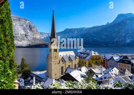 Schöne sonnige Stadtlandschaft der besonderen Stadt Hallstatt in Österreich Salzkammergut verschneite Winterberge und See und Kirche. Stockfoto