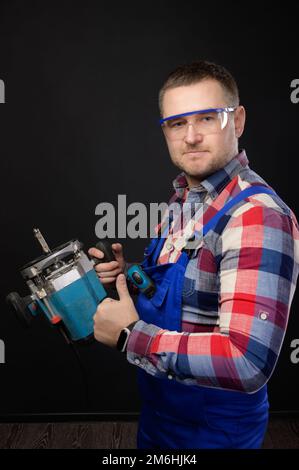 Ein weißer Handwerker in Brille mit Holzbearbeitungswerkzeugen in der Hand zeigt Daumen nach oben. Porträt eines Zimmermanns auf einem schwarzen Studio-Bac Stockfoto