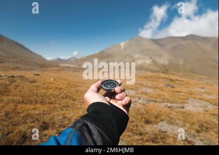 DIE Hand eines männlichen Reisenden hält einen magnetischen Kompass vor der Kulisse einer Bergregion. Orientierung und den Weg finden Stockfoto