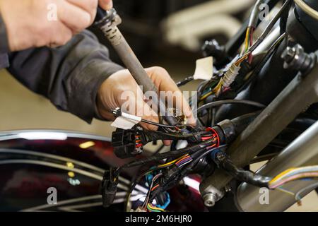 Ein Elektriker lötet elektrische Drähte an elektrische Geräte in einem Motorrad. Nahaufnahme. Transportkonzept Stockfoto