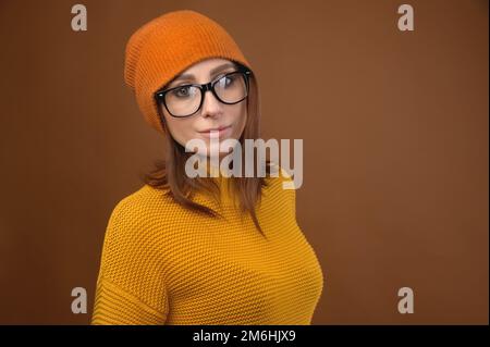 Die attraktive kaukasische Frau mittleren Alters, die einen gelben Pulli mit Hut und Brille trägt, schaut auf die Kamera. Vision Problem und Menschen müde Stockfoto