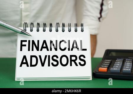 Geschäftskonzept. Auf einer grünen Oberfläche steht ein Taschenrechner, ein Mann zeigt mit einem Stift auf ein Notizbuch mit der Aufschrift "Finanzberater" Stockfoto