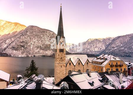 Wunderschönes Stadtbild der besonderen Stadt Hallstatt in Österreich Salzkammergut verschneite Winterberge und See und Kirche bei Sonnenuntergang. Stockfoto