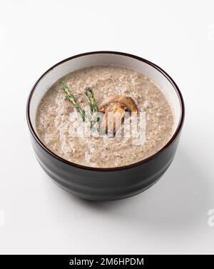 Cremesuppe aus Champignons mit Thymian in einer Keramikschüssel auf weißem Hintergrund. Der Begriff der vegetarischen und diätetischen Nahrung. Draufsicht. Stockfoto