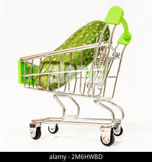 Ein Miniatur-Supermarkt-Wagen mit einer falschen grünen Gurke. Stockfoto
