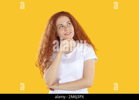 Porträt eines denkwürdigen Rothaarigen im weißen T-Shirt, das auf gelbem Hintergrund nach oben schaute und das Kinn berührte. Stockfoto