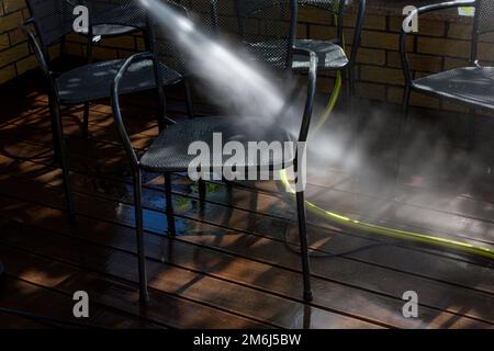 Leistungsstarke Oberflächenreinigung. Ein Mann, der die Terrasse mit einem Hochdruckreiniger reinigt. Hochdruckreiniger auf Holzterrasse und Gartenmöbeln. Stockfoto