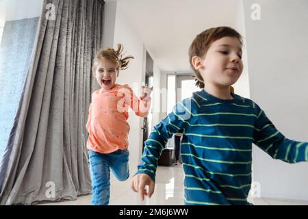 Glückliche Familie, die im Flur läuft. Lustige Kinder, die mit einer Schachtel springen, Eltern, die lachen, Stockfoto