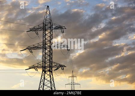 Silhouetten von Hochspannungstürmen mit elektrischen Drähten im Hintergrund des Sonnenuntergangs und der Wolken. Stromübertragungsleitungen, Stromversorgungskonzept Stockfoto