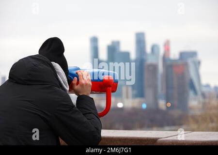 Mann, der ein Fernglas benutzt, um das Panorama der Stadt Moskau zu betrachten. Touristen auf der Aussichtsplattform im Winter Stockfoto