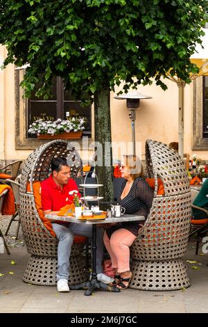 Gäste, die in Dresden, Sachsen, im Schatten eines Baumes im Freien in Korbstühlen sitzen, genießen ruhige Drinks und Mittagessen Stockfoto