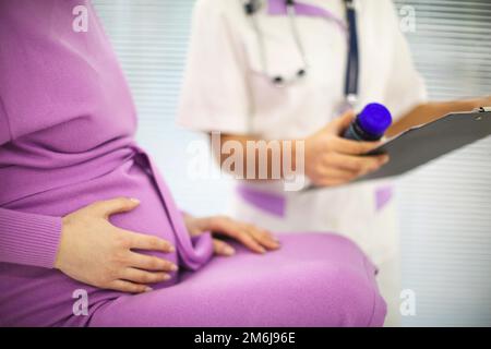 Wunderschöne junge gemischte Rasse weibliche Ärztin mit schwangere Patientin vor dem Teilnehmer, Tablettenbehälterhalter Stockfoto
