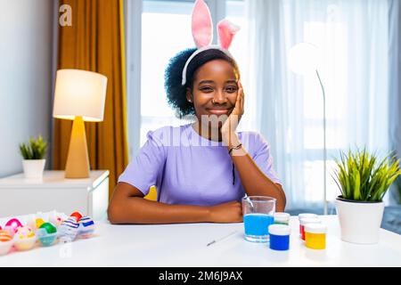 Glückliche Frau mit Häschenohr, die Eier in der Wohnung malt und sich auf ostern vorbereitet Stockfoto