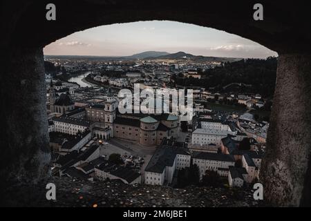 Ein Fenster mit Blick auf eine Burg einer Stadt in Salzburg, Österreich, bei Sonnenuntergang. Stockfoto