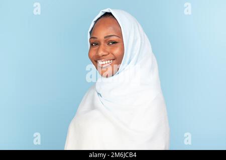 Porträt einer wunderschönen schwarzen muslimischen Frau im Hijab, posiert auf blauem Studiohintergrund, lächelt vor der Kamera, kopiert Stockfoto