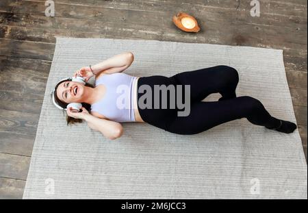 Bild einer erstaunlich gesunden schwangeren Frau zu Hause auf dem Sofa, die Musik mit Kopfhörern hört Stockfoto