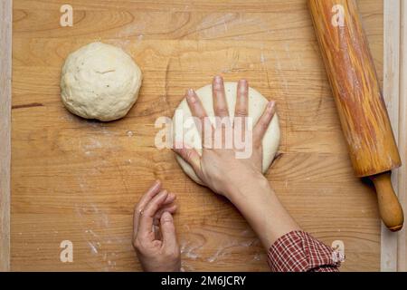 Ein flaches Foto, auf dem ein kleiner Teigball mit dem Rollnadel ausgerollt wird. Stockfoto