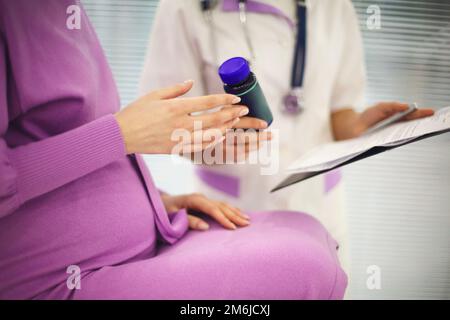 Wunderschöne junge gemischte Rasse weibliche Ärztin mit schwangere Patientin vor dem Teilnehmer, Tablettenbehälterhalter Stockfoto