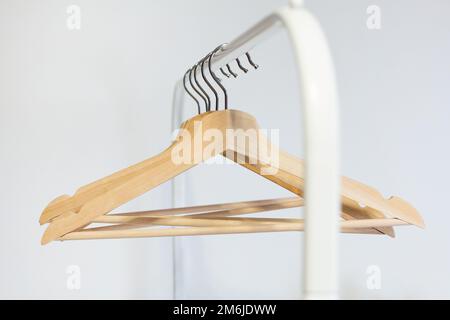 Ein Holzbügel hängt an einer Edelstahlschiene in einem Raum mit weißen Wänden Stockfoto