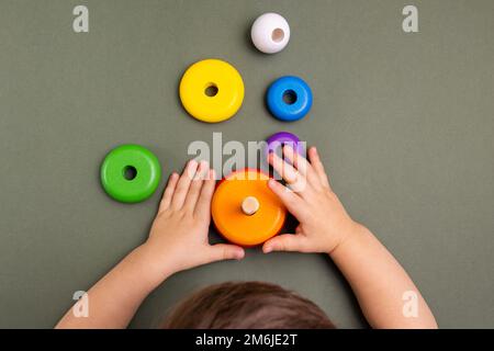 Nahaufnahme eines kleinen Babys im Pyjama, das mit der Holzpyramide auf grünem Hintergrund spielt. Natürliches umweltfreundliches Spielzeugkonzept. Stockfoto