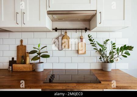 Küchenutensilien aus Messing, Küchenzubehör. Hängeküche mit weißen Fliesen an der Wand und Holztisch. Grüne Pflanze auf Küchenrückseite Stockfoto