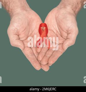 Rote Schleife auf mans zur Sensibilisierung der Hände auf grünem Hintergrund. HIV, AIDS Welttag. Das Konzept der sozialen Lebensfragen. Ki Stockfoto