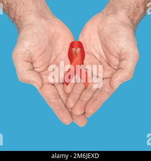 Rote Schleife mit Farbband auf mans, um die Hände auf blauem Hintergrund zu isolieren. HIV, AIDS Welttag. Das Konzept der sozialen Lebensfragen. Hilfe Stockfoto