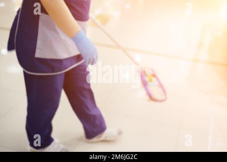 Eine Putzfrau in blauer Uniform und Handschuhen wäscht einen Fliesenboden mit einem Mopp. Verschwommenes Bild Stockfoto