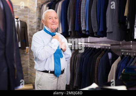 Älterer Mann, der im Bekleidungsgeschäft Krawatte wählte und versuchte Stockfoto