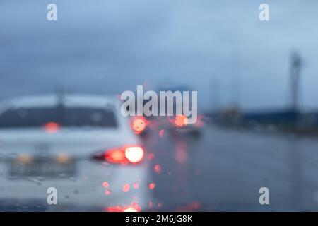 Verschwommene Sicht durch die nasse Windschutzscheibe von Autos, die an einem bewölkten Tag die Straße entlang fahren Stockfoto