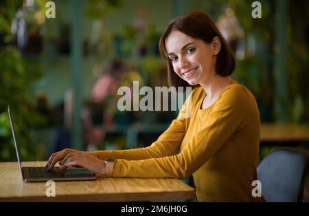 Geschäftsfrau mit seitlichem Blick, die auf dem Laptop sitzt, während sie im Café sitzt Stockfoto