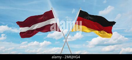 Zwei überkreuzte Flaggen Bundesrepublik Deutschland und Lettland winken im Wind am bewölkten Himmel. Beziehungskonzept, Dialog, Reisen zwischen zwei Ländern Stockfoto