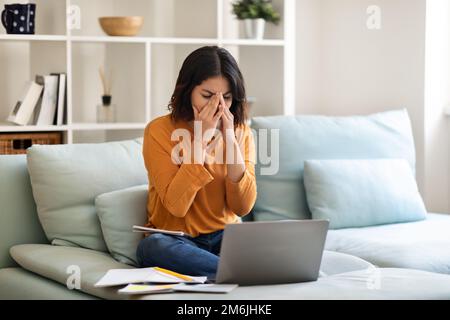 Gestresste Junge Arabische Frau, Die Sich Müde Fühlt, Während Sie Zu Hause Mit Einem Laptop Lernt Stockfoto