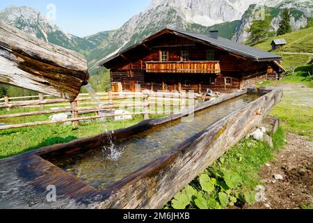 alpenkabine und Wassertrog am Fuße des Dachsteins im Alpendorf Neustatt Alm in den österreichischen Alpen in Steiermark Stockfoto