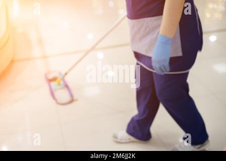 Eine Putzfrau in blauer Uniform wäscht einen Fliesenboden mit einem Mopp. Unschärfe-Effekt Stockfoto