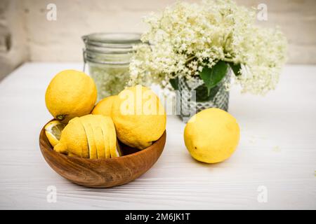 Frische Holunderbeerblüten für die Zubereitung eines erfrischenden Sommergetränks mit Zitrone. Eco-Teller mit gelben hässlichen Bio-Zitronen auf dem Tisch Stockfoto