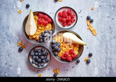 Golden Cornflakes mit frischen Früchte Himbeeren, Heidelbeeren und Birne in Keramik Schüssel Stockfoto