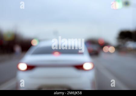 Ein weißes Auto mit eingeschalteten Scheinwerfern fährt bei bewölktem Wetter die Straße entlang. Unschärfe-Effekt. Stockfoto