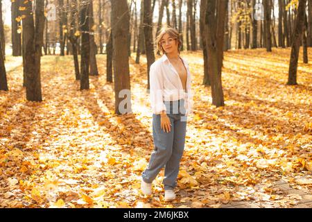 Porträt eines jungen, fantastischen Teenagers, das an einem sonnigen Herbsttag im Park zwischen Bäumen auf gelben Ahornblättern steht. Stockfoto