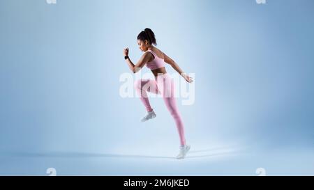 Seitenansicht der fit Black Lady beim Training, Laufen auf blauem Studiohintergrund, kostenloser Kopierbereich, Panorama Stockfoto