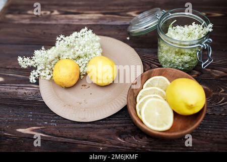 Zutaten für die Zubereitung eines Getränks aus Holunderbeeren und Zitronen. Zitronenscheiben und frische Holunderblüten für den Winter. Stockfoto