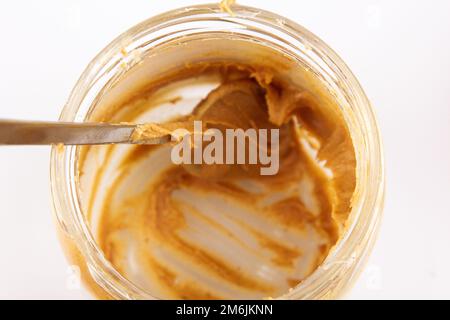 Erdnussbutter in einem offenen Glas. Leerer Erdnussbutter-Behälter. Der letzte Löffel voller köstlicher Pasta-Snacks Stockfoto