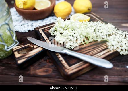 Zerkleinern von Zitrone und schwarzer Holunderbeere auf einem Schneidebrett zur Herstellung eines Kräutergetränks oder eines Medikaments zur Heilung von Sirup aus Holunderblüten zu Hause. Stockfoto